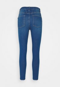 Pantalones vaqueros ajustados en denim azul oscuro, con una textura suave, diseño tradicional de cinco bolsillos y detalles de costura sutiles en la parte trasera.