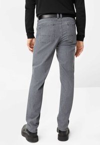 Graue Jeanshose mit geradem Bein, ausgestattet mit zwei Gesäßtaschen und einem schwarzen Gürtel, getragen mit einem langärmligen schwarzen Hemd.