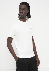 Λευκό βαμβακερό t-shirt με κοντά μανίκια, στρογγυλή λαιμόκοψη και μικρό μαύρο λογότυπο στο αριστερό στήθος. Λεια υφή, άνετη εφαρμογή.