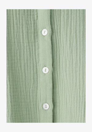 Jasnozielony, teksturowany materiał z pionowymi paskami posiada białe guziki wzdłuż środka. Materiał wydaje się miękki i lekki.