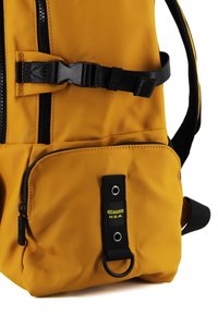 Zaino in nylon giallo con accenti neri, dotato di un ampio scomparto principale, tasca frontale con zip e una tracolla nera con un anello metallico.