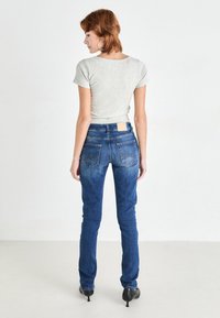 T-shirt gris à manches courtes associé à un jean en denim foncé, moulant, avec un léger patch sur la taille et deux poches arrière.