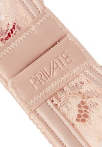 Zbliżenie na różową koronkową bieliznę z wyhaftowanym napisem "PRIVATE" na gładkim pasku blisko metalowej sprzączki.