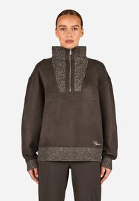 Tmavo hnedý pulóver so zipsom a vysok�ým golierom, ktorý má textúrovaný predný panel a rebrovaný spodný okraj a manžety v kontrastnom bodkovanom materiáli.