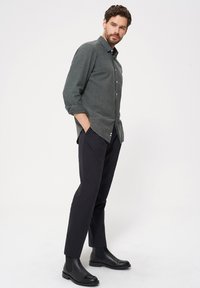 Szary koszula z guzikami w teksturowanej tkaninie, zestawiona z czarnymi slim-fit spodniami i czarnymi botkami za kostkę, prezentująca nowoczesny i elegancki design.