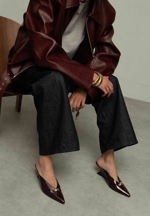 Muiltjes in donker bordeauxrood leer met een spits toelopende neus en een kleine sleehak, voorzien van een gouden metalen accent op de wreef.