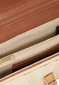 Sac à main en cuir marron avec une finition texturée. L'intérieur présente un doublure en lin beige et une poche zippée avec des accessoires en or. Base tissée à rayures.