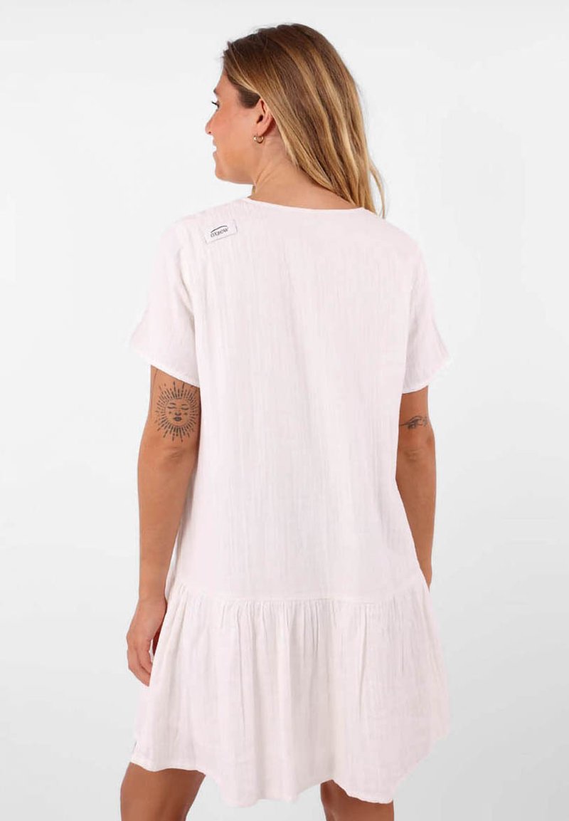 Robe blanche à manches courtes avec un design fluide, présentant un ourlet froncé. Fabriquée en tissu léger, comprend une étiquette près de l'encolure.
