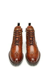 Stivali in pelle marrone con lacci, caratterizzati da un design wingtip, dettagli perforati, punta rotonda e linguette nere. Suola in gomma testurizzata.
