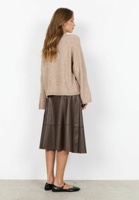 Ljusbeige stickad tröja, lös passform, över en mörkbrun läder A-linjeformad kjol med horisontella sömdetaljer. Platta svarta skor fulländar outfitten.