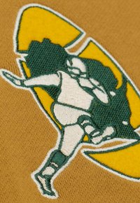 Grafica ricamata di un giocatore in bianco e verde su uno sfondo beige, con un accento giallo che presenta un design circolare e una posa dinamica.