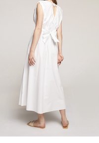 Bílé bezramenné šaty s mašlí na zádech, výstřihem do V a volným střihem. Vyrobené z lehkého materiálu.