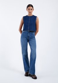 Top sin mangas de mezclilla con dobladillo deshilachado, combinado con jeans azules acampanados de cintura alta. Ambos presentan un lavado azul clásico y un detalle mínimo.
