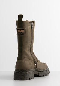 Bottes basses en cuir vert olive avec fermeture éclair latérale, finition texturée, semelle en caoutchouc noire épaisse et patch de marque sur le talon.