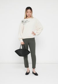 Lichtbeige sweatshirt met bloemenomlijsting, olijfgroene fitted broek, zwarte gestructureerde handtas en zwarte flats. Minimalistische stijl.