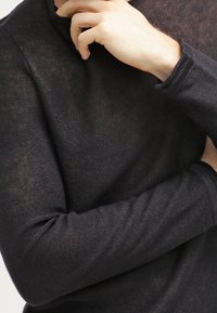 Černý dlouhý rukáv top s lehkým, texturovaným pletením. Obsahuje kulatý výstřih a přiléhavé rukávy, které vykazují jemnou, průsvitnou kvalitu.