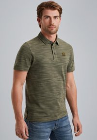 Polo vert olive avec un motif texturé et rayé, patte de boutonnage à trois boutons, et un écusson de marque sur la poitrine gauche. Coupe décontractée.