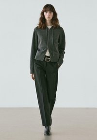 Gray zip-up sweater, cream shirt underneath, black high-waisted trousers, black ankle boots, and minimalistic design.