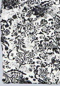 Stoff mit floralem Muster in Schwarz und Weiß, mit Knöpfen und einer Tasche. Das Material hat eine glatte Textur mit detaillierten botanischen Motiven.