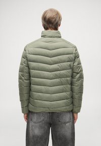 Ελαιόχρωμο μπουφάν με καπιτονέ σχέδιο σε τετράγωνες ρίγες, ψηλό γιακά και λαστιχένιες μανσέτες, με λεία, γυαλιστερή υφή υφάσματος.