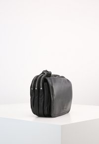 Černá kožená taška s kompaktním obdélníkovým tvarem, která má tři zipové přihrádky a hladkou texturu. Minimalistický design.