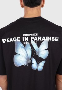 Black t-shirt featuring large blue butterfly graphics on the back and white text stating "DROPSIZE PEACE IN PARADISE EST. 2020".