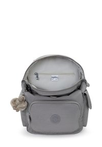 Sac à dos Kipling gris clair avec poche zippée à l'avant, compartiment principal ouvert montrant une poche zippée intérieure, et un petit porte-clés en peluche en forme de singe.