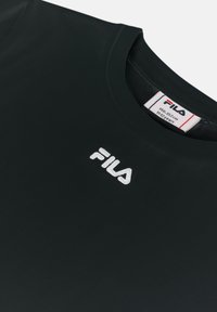 Camiseta negra de cuello redondo hecha de una tela suave, con el logotipo bordado en blanco de "FILA" en el pecho. La etiqueta indica la talla para niños.