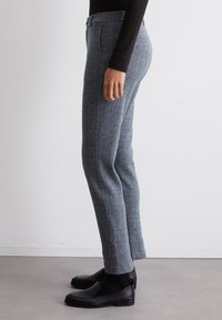 Pantalons gris en motif chevrons fabriqués dans un tissu texturé, dotés de poches latérales et d'une coupe ajustée, associés à des chaussures noires à enfiler.