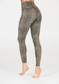 Vrouw in hoge taille legging met luipaardprint, blootvoets op de tenen staand tegen een effen witte achtergrond.