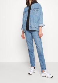 Ljusblå denimjacka med klassisk design, knappstängning och bröstfickor, i kombination med matchande ljusblå jeans och vita sneakers.