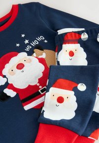 Marineblå fleece-sæt bestående af top og bukser med røde kanter, designet med Sankt Nicolaus, der har hvide skæg, røde næser og jule-akcenter. Blød tekstur.