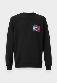 Zwarte sweatshirt met lange mouwen, ribgebreide manchetten en ronde hals. De voorkant heeft een multicolor "tommy JEANS" logo patch. Zacht katoenmateriaal.