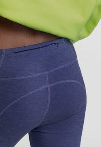 Marineblauwe leggings van rekbare stof, met een kleine ritszak aan de achterkant en contrasterende gebogen stikdetails.
