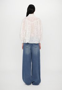 Blusa bianca e trasparente con un motivo floreale e maniche a sbuffo, abbinata a pantaloni in denim blu chiaro a vestibilità comoda.