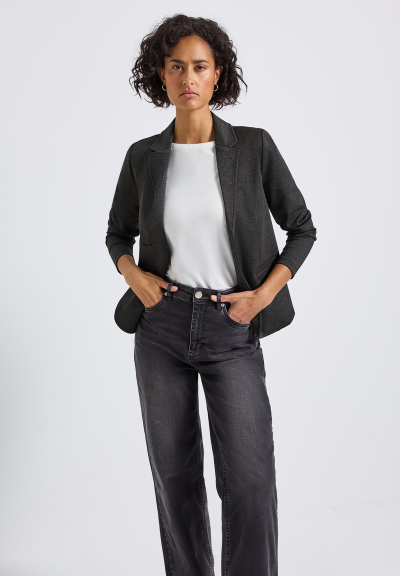 Ciemnoszary żakiet z wyłogami, długimi rękawami i kieszeniami, stylizowany na białą koszulę i zestawiony z czarnymi dżinsami z wysokim stanem.