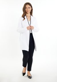 Cardigan alb, cu deschidere în față, cu guler tip șal și margini negre, asortat cu pantaloni negri și mulați și tocuri negre cu vârful ascuțit. Textură netedă.