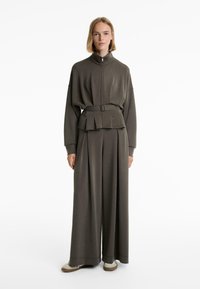 Dark green oversized jacket with zip and belt, paired with wide-leg pants. Both pieces feature a soft texture and simple design.
