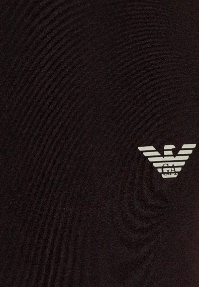 T-shirt en coton noir avec un tissu texturé, arborant un petit logo d'aigle à rayures blanches horizontales sur la zone gauche de la poitrine.