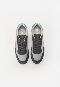 Baskets grises et noires avec un design en maille, lacets ronds, un accent bleu au talon et une semelle intérieure rembourrée avec un logo visible.