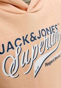 Breskvasta kapuca z napisom "JACK & JONES Superior" v temno modri in beli barvi, z oznako "Since 1990" v spodnjem kotu.