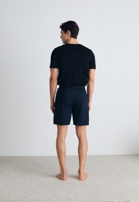 Camiseta negra de manga corta y pantalones cortos azul marino, de material de algodón, diseño minimalista, de pie sobre una alfombra texturizada clara.