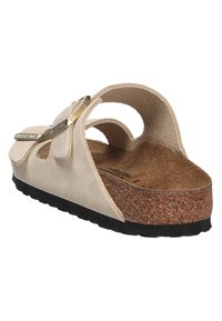 Beige suede sandal with two straps, cork footbed, and black rubber sole. Metallic accents on straps add detail. Lightweight design for comfort.