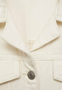 Détail du col en denim crème avec bouton-pression en métal, coutures visibles et tissu texturé.