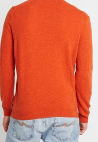 Orange stickad tröja med långa ärmar, rundad halsringning och ribbade ärmslut. Texturen ser mjuk ut, med ett subtilt melerat mönster.