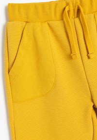 Gelbe Sweatpants aus geripptem Stoff mit elastischem Bund, Kordelzug und Seitentaschen. Strukturierte Oberfläche und leuchtende Farbe.