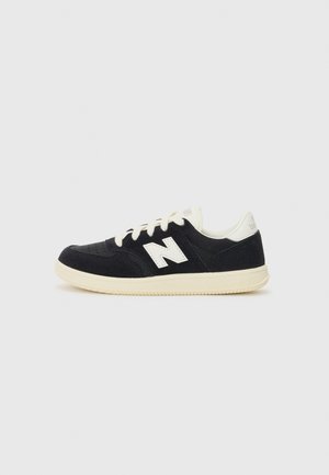 Baskets en daim noir avec des accents blancs, bout perforé, lacets ronds et semelle en caoutchouc texturé. Logo New Balance sur le côté.