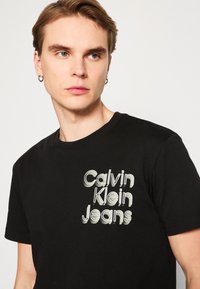 Calvin Klein Jeans STACKED EUPHORIC LOGO TEE - Camiseta estampada - black