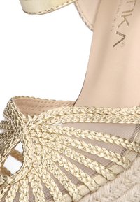 Sandalia de espadrille trenzada en dorado que presenta una parte superior tejida, detalles de malla y una plantilla suave en beige. Ligera, con un diseño de plataforma.