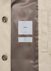 Beige jackas insida med en slät brun foder, som har en metallknapp och etiketter för varumärke och vattenavvisande egenskaper.